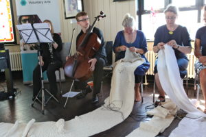 Photograph of several people, a man with a double bass,and women sewing