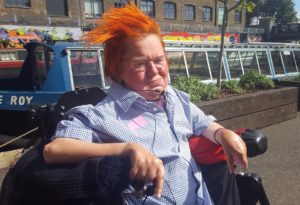 a woman with orange hair sits in her wheelchair in front of a canal boat